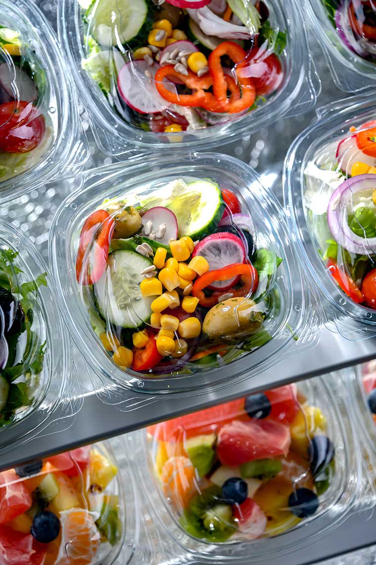 A variety of colorful salads in clear plastic containers on a metallic surface.