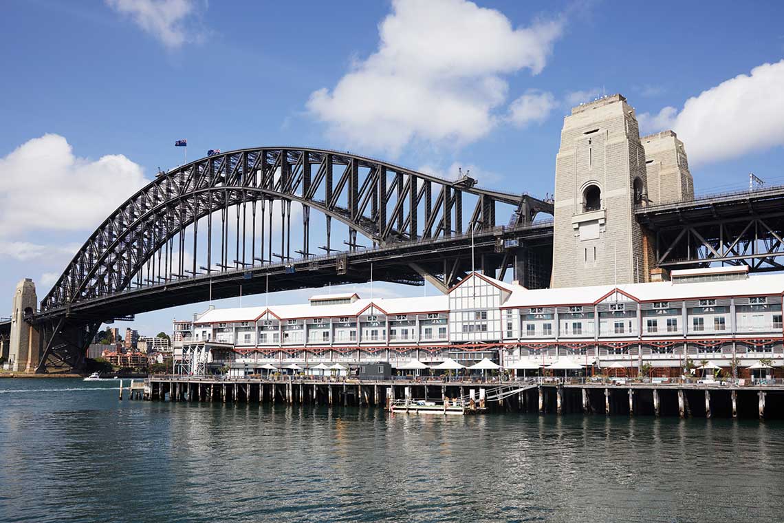 Sydney Harbour Bridge with a waterfront building beneath a blue sky.